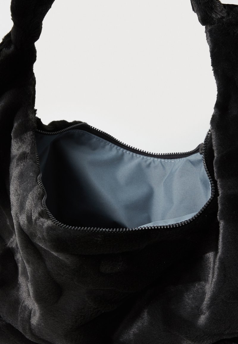 Borsa in pelliccia sintetica nera con chiusura a zip. L'interno è foderato in un morbido tessuto blu. Presenta una texture morbida e due manici robusti.