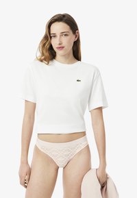 T-shirt bianco corto con maniche corte, con un piccolo logo verde. Perizoma in pizzo rosa chiaro con una cintura solida, abbinato a un indumento rosa.