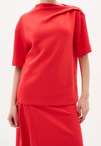 Rode katoenen blend top met een relaxte pasvorm, korte mouwen en een asymmetrische halslijn, gecombineerd met een bijpassende rok.