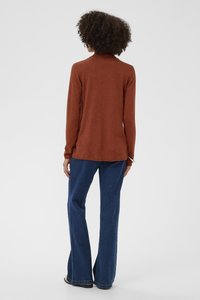 Rozsda színű, hosszú ujjú pulóver magas nyakkal, bővülő kék farmerhez párosítva. Egyszerű, hétköznapi kialakítás, sima textúrával.