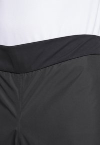 Shorts noirs avec une texture lisse et une taille élastique, dotés d'un panneau en mesh blanc au-dessus. Pas de motifs visibles ni de détails matériels.