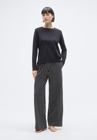 Haut noir à manches longues associé à un pantalon à jambes larges rayé noir et blanc. Matière en coton ; coupe décontractée avec un design minimaliste.