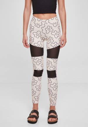 Leggings avec un motif floral en crème et noir, présentant des panneaux en maille noire transparente sur les cuisses. Tissu lisse, design ajusté.