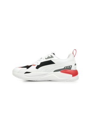 Des chaussures de sport blanches avec un panneau en maille noire, un accent rouge au talon et des détails gris. Semelle texturée avec une traction en caoutchouc prononcée.