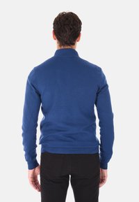 Maglione blu lavorato a maglia con un design aderente, maniche lunghe e orlo a coste, abbinato a pantaloni scuri. Nessun motivo o accento visibile.