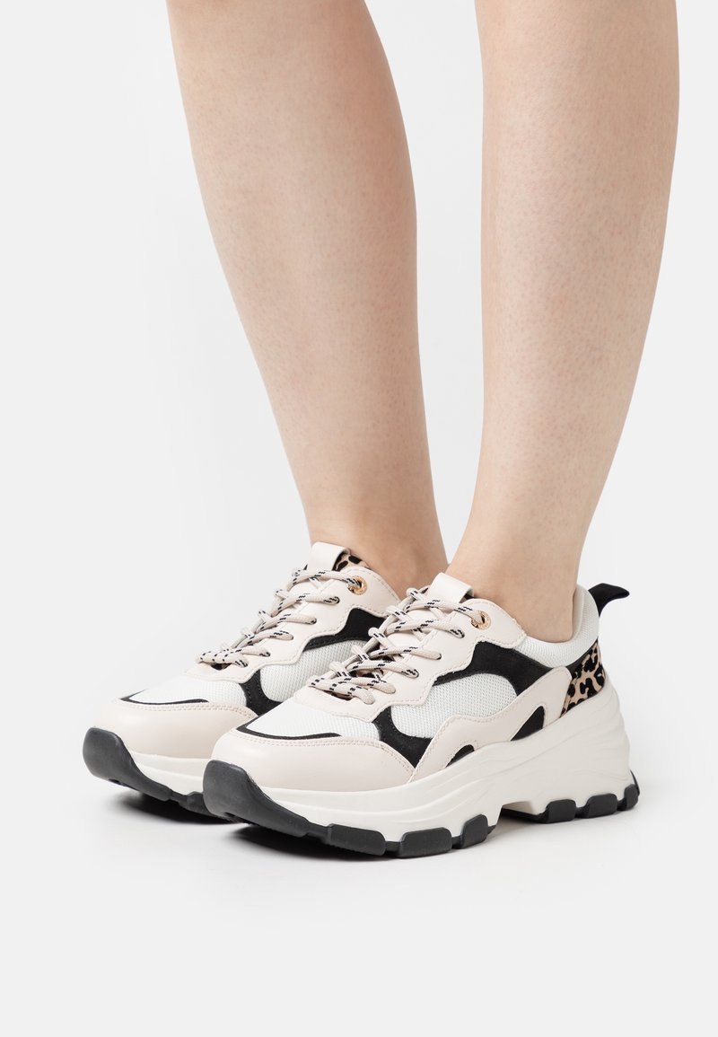 Baskets chunky en crème, noir et imprimé léopard. Comprennent des panneaux en mesh, des semelles en caoutchouc noir et des œillets métalliques pour les lacets.