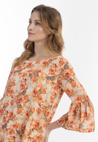 Blomstret bluse med lange, udfoldede ærmer; prydet med orange, rød og grå mønstre på en cremet baggrund; letvægts, struktureret stof.