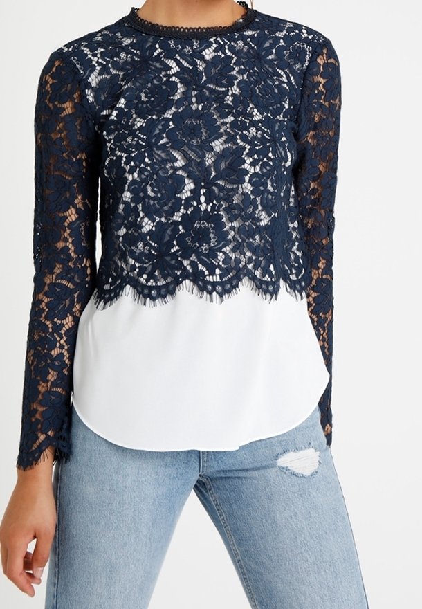 Marinblå blommig spets långärmad topp lager över vit tyg, tillsammans med ljusblå slitna jeans.