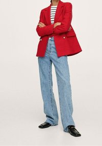 Blazer rouge texturé à double boutonnage, associé à un jean en denim bleu clair taille haute. Des mocassins noirs complètent le look.