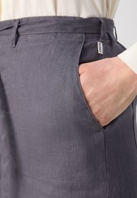Sive lanene hlače z stransko žepom in etiketo. Gladka tekstura s subtilnim tkanjem, oblikovane s ravnim krojem za moderni fit.