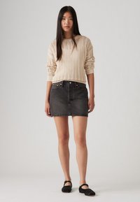 Pull en crème tricoté avec un motif texturé, associé à une jupe en denim noire ajustée et des chaussures plates noires avec un détail de bride.