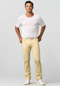 Beige cargopants met een slim fit en een gestructureerd wit T-shirt. Gecombineerd met witte high-top sneakers, bestaat de outfit uit een lichtgekleurde riem.