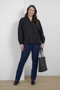Camisa negra de manga larga con botones y cuello rizado, combinada con jeans azules y botines negros de tacón, sosteniendo un bolso tote negro.
