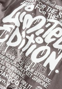 T-shirt en coton gris avec des graphiques blancs audacieux, utilisant différentes polices et phrases, transmettant des messages sur l'authenticité et la confiance.