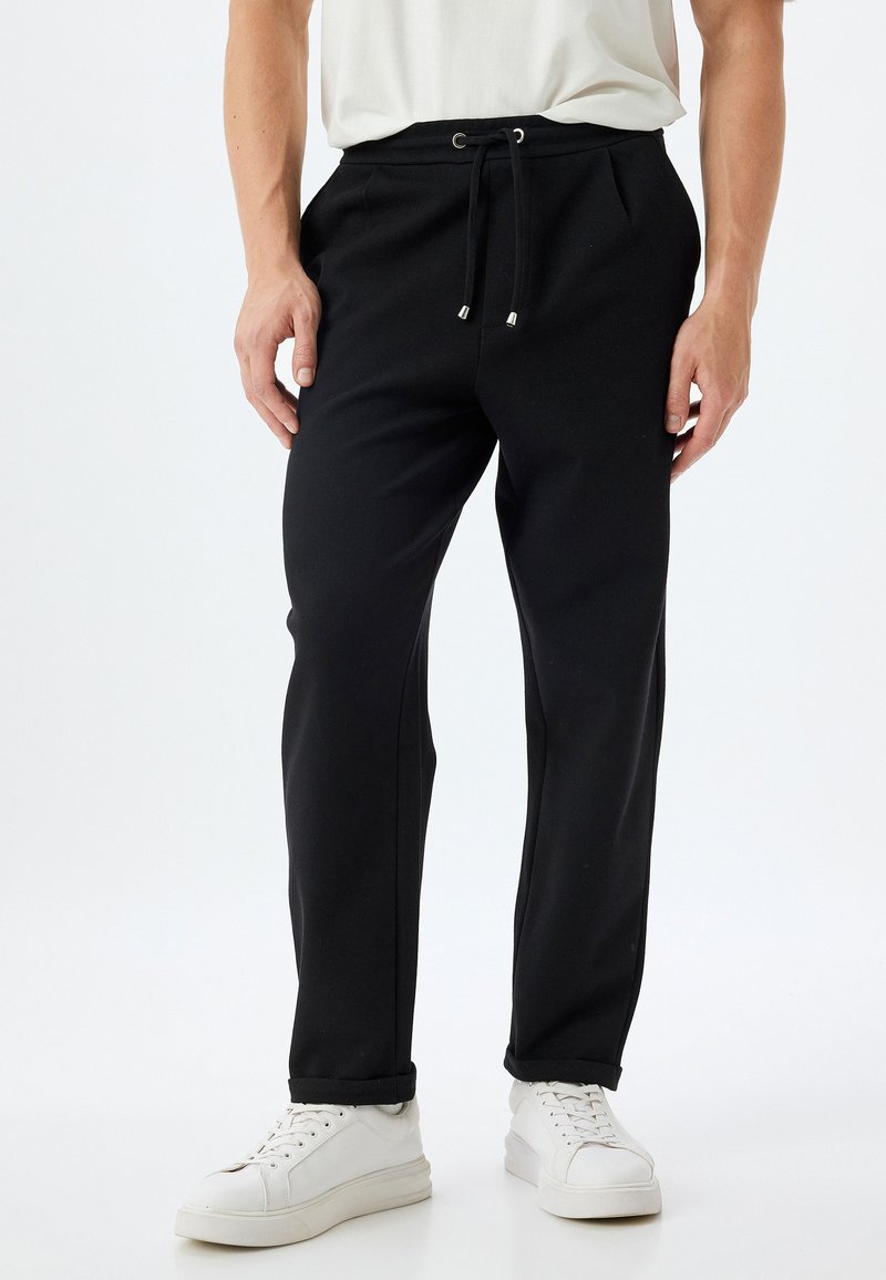 Pantalones deportivos negros hechos de una tela suave y elástica. Cuentan con una cinturilla elástica con cordón ajustable y un diseño de pierna ajustada.