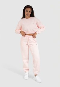 Lichtroze cropped sweatshirt en bijpassende sweatpants van zacht materiaal. De broek heeft elastische manchetten en een klein logodetail bij de tailleband.