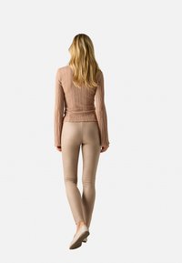 Top de manga larga de color rosa claro con relieve y mangas acampanadas, acompañado de leggings ajustados color beige. El conjunto tiene una textura suave y un ajuste estilizado.