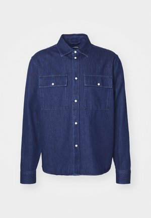 Camicia in denim scuro con colletto a punta, due taschini sul petto e maniche lunghe. Presenta bottoni bianchi e una leggera texture.