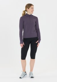 Pitkähiha, vetoketjullinen paita tumman violetista kankaasta, yhdistetty mustiin capri-leggingseihin ja harmaanvärisiin lenkkikenkiin. Sujuva pinta, tiukka muotoilu.