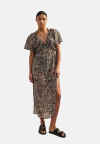 Maxi-jurk met luipaardprint, korte mouwen en een diepe V-halslijn, met een zijsplit. Gepaard met zwarte sandalen.