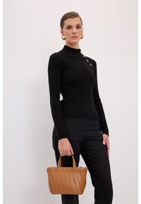 Pull noir à côtes avec un col montant et un détail de boutons dorés, associé à un pantalon noir ajusté et un sac en cuir plissé couleur beige.