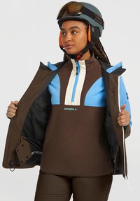 Bruine fleece pullover met blauwe en crèmekleurige accenten, kwart-rits voorkant, gedeeltelijk opengezipte jas, gestroomlijnd helm met bril, en gestructureerde stof.