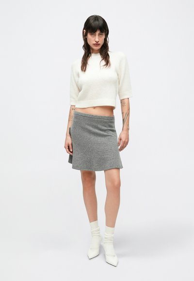 Szara dzianinowa spódnica o rozkloszowanym kroju w połączeniu z białym krótkim swetrem. Do tego białe skarpetki do kostki i białe, spiczaste buty.