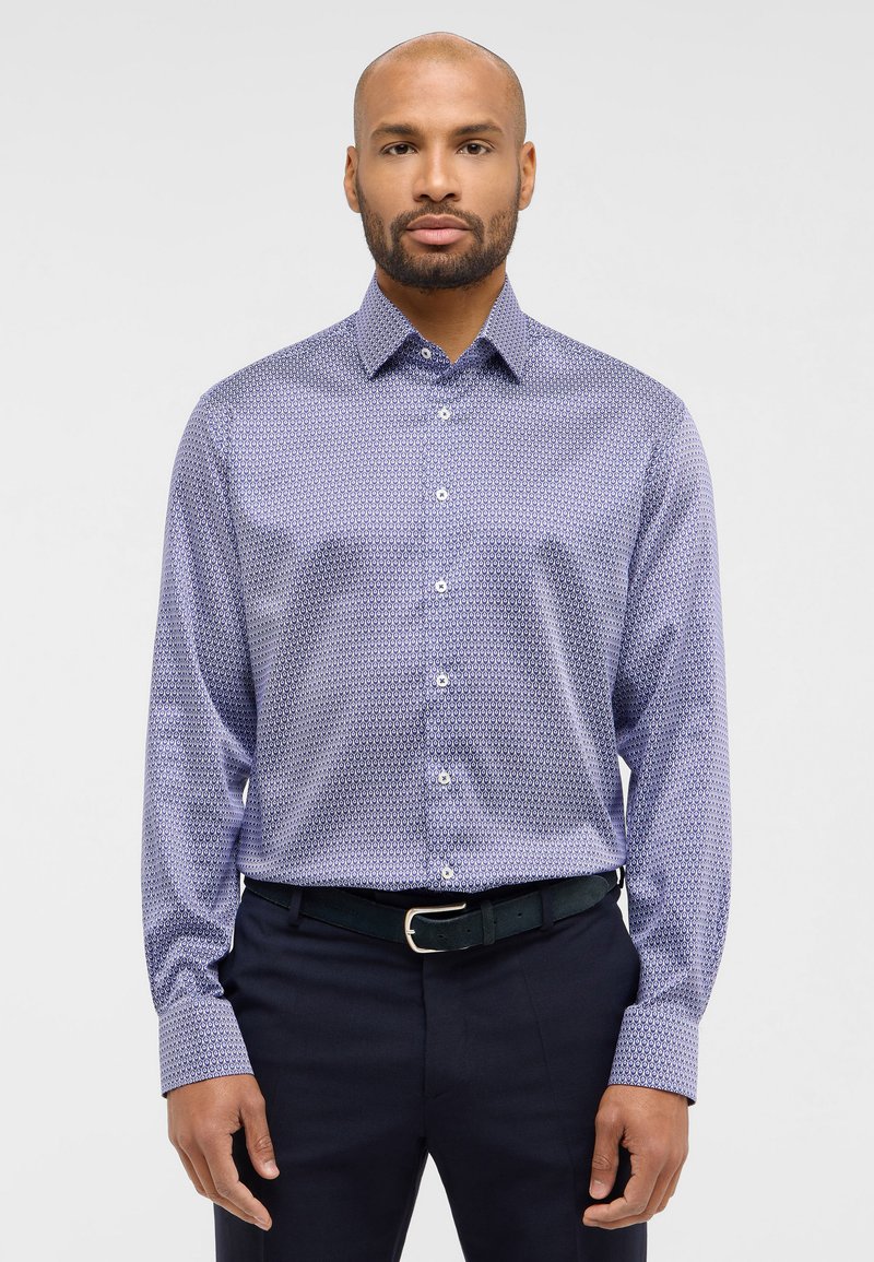 Lange mouwen shirt in paars met een geometrisch patroon, knoopsluiting aan de voorkant en een gespreide kraag, gecombineerd met donkere broek en een zwarte riem.