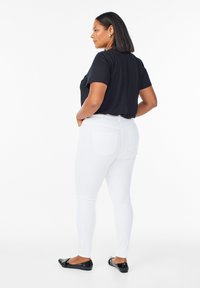 Camisa negra de manga corta combinada con jeans ajustados blancos y unas bailarinas negras. El atuendo presenta un diseño sencillo y ajustado, con texturas de tela suaves.