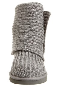 Bota de tobillo gris de punto con patrón texturizado, que cuenta con un puño vuelto y suela de goma plana. Material de tela suave.