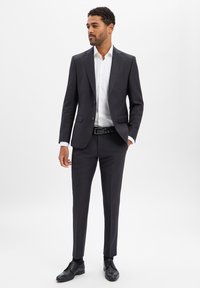 Dark tailored suit with a single-breasted jacket, white shirt, and black belt. Smooth fabric, slim fit, and polished black shoes.