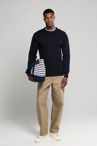 Suéter azul marino con cuello redondo y botones en los hombros; pantalones beiges; llevando un bolso a rayas azul marino y blanco; zapatillas ligeras.