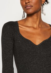 Black ribbed knit top with a deep V-neck and long sleeves, featuring metallic flecks. The model wears silver triangular earrings.