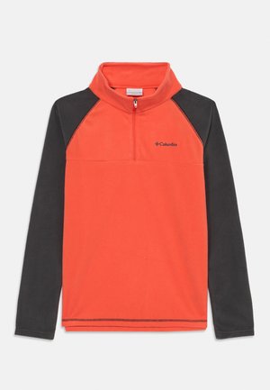Pull en polaire orange vif avec des manches raglan noires, col zippé à moitié et logo brodé sur la poitrine. Texture douce.