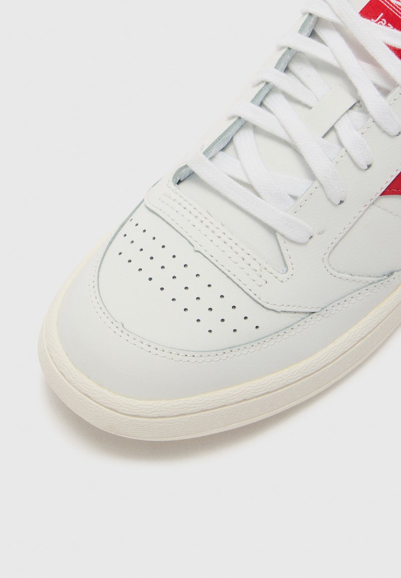 Sneaker bianca in pelle con punta forata, suola bianca testurizzata e accento rosso sul lato. Caratterizzata da lacci bianchi e una finitura liscia.