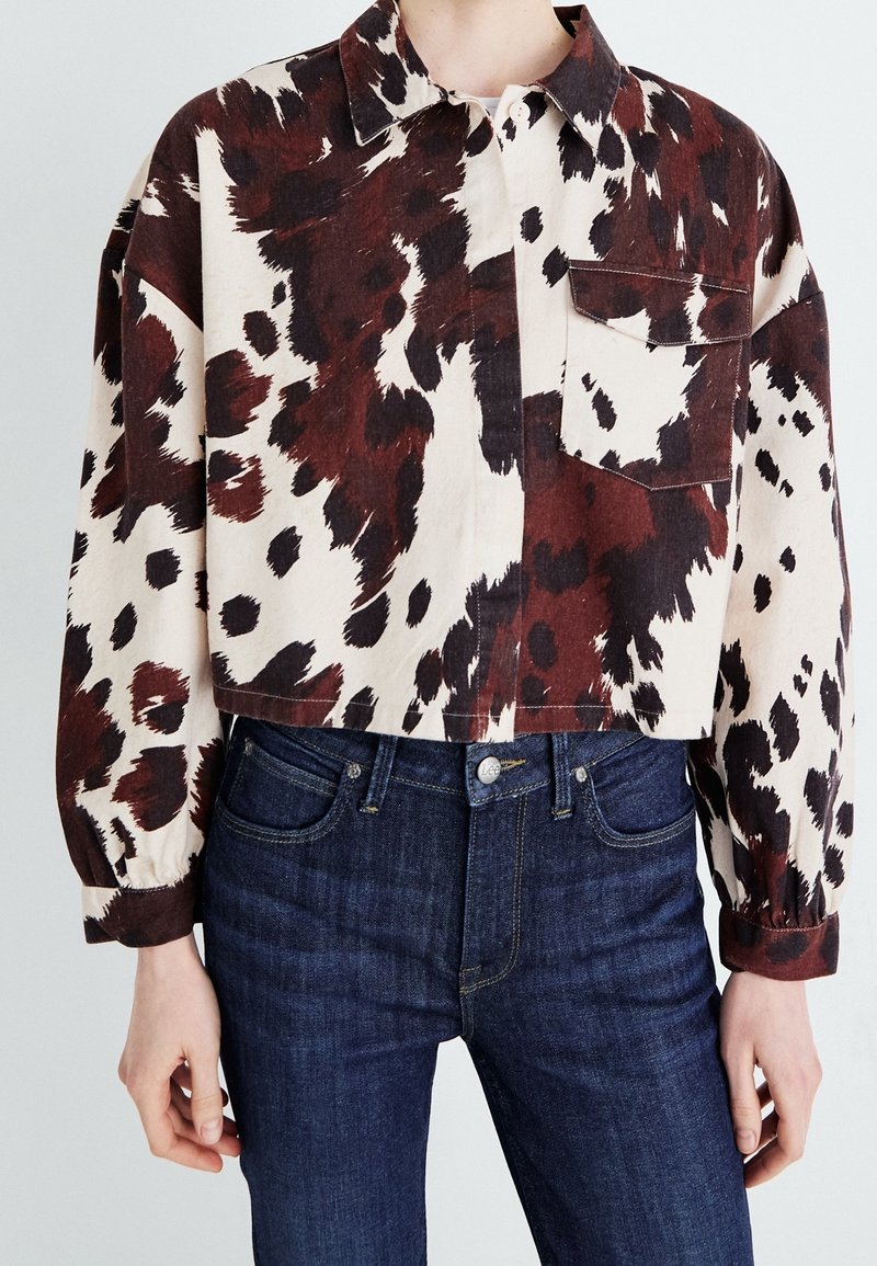 Veste courte boutonnée avec imprimé animal abstrait marron, noir et crème portée avec un jean bleu foncé.
