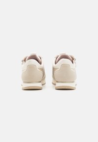 Béžové a bílé semišové sneaker s tkanými bočními panely, pohled z jejich zadní části na bílém pozadí.