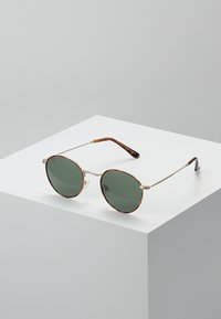 Ochelari de soare rotunzi cu lentile verzi, cadru subțire din metal argintiu și brațe cu model țestoasă. Design minimalist pe un fundal alb.