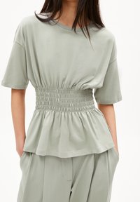 Světlá zelená peplum halenka s nařaseným pasem, krátkými rukávy a jemnou, strukturovanou tkaninou. Ležérní design s uvolněným střihem.