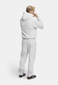 Lys grå hoodie i bomuldsblanding med en rummelig hætte, parret med matchende sweatpants. Sorte og hvide sneakers fuldender outfittet.