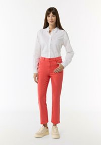 White button-up shirt paired with coral pants and beige sneakers. Pants feature a slim fit and front pockets. Smooth, lightweight fabric.