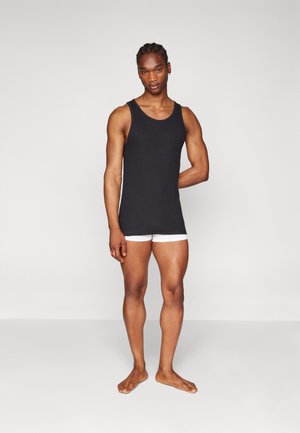 Schwarzes Tanktop mit rundem Ausschnitt, kombiniert mit weißen Boxershorts. Der Stoff hat eine glatte Textur und passt eng am Körper.