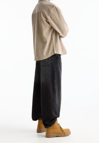 Camisa de pana beige, pantalones de mezclilla negros y botas amarillas de cordones con suela texturizada. El conjunto presenta un ajuste relajado y costuras visibles.