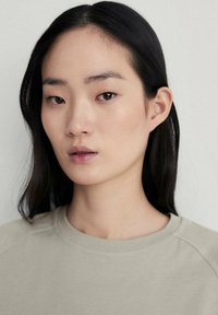 Svetlá béžová mikina, s okrúhlym výstrihom, so hladkým povrchom a mierne voľným strihom. Model má priamé tmavé vlasy a neutrálny make-up.