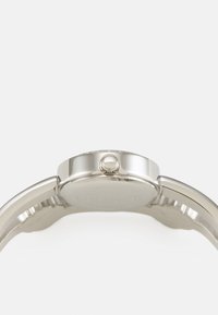Silver watch with a smooth metal finish, round case, and textured crown. The strap features a polished surface and subtle grooves.