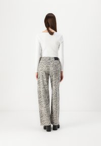 Pantalones de pierna ancha con estampado de cebra en gris y blanco, hechos de algodón, con cintura alta y un detalle de bolsillo trasero. Etiqueta negra cerca de la cintura.
