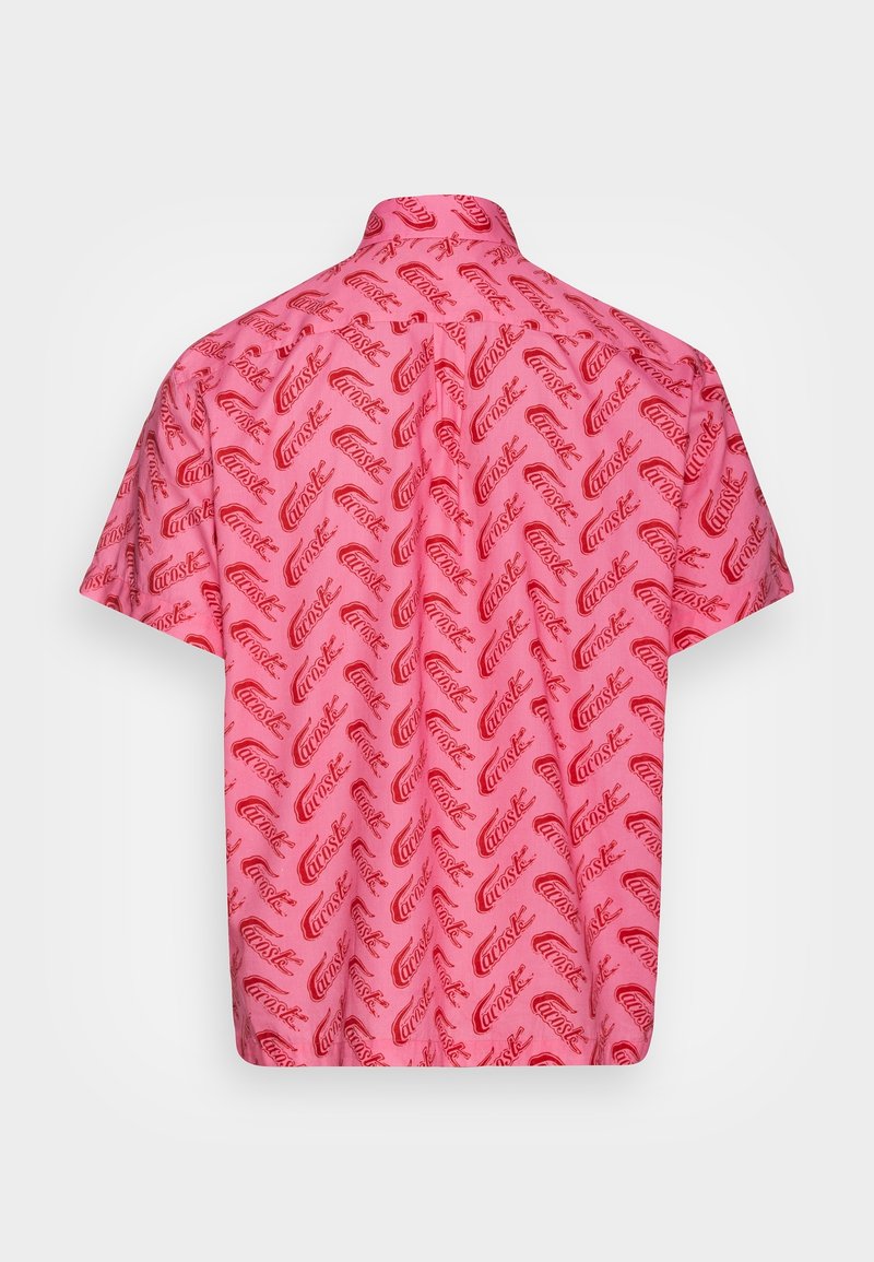 Chemise rose à manches courtes avec motif répétitif de texte rouge en diagonale "Carostak", vue de dos sur fond blanc uni.