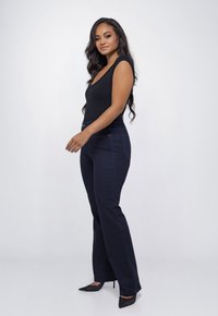 Zwarte, nauwsluitende bodysuit, donkerblauwe high-waisted flared jeans, gladde denimtextuur, subtiele ontwerpelementen, zwarte stilettos, model kijkt naar links.