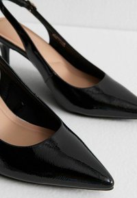 Escarpins à talons slingback en cuir verni noir avec des pointes effilées et une finition brillante. Ces chaussures présentent un design épuré et un talon fin pour un profil élégant.