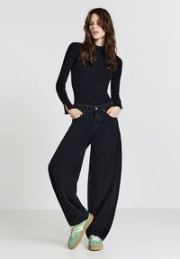 Schwarzes, geripptes Langarmoberteil, hochtaillierte, weit geschnittene schwarze Jeans und grüne Sneakers mit beigen Sohlen. Minimalistisches Design mit subtiler Textur.